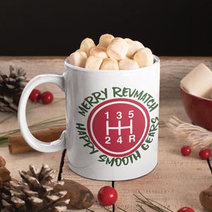 Könnte beinhalten: Weiße Keramiktasse mit einem roten und grünen Design. Das Design zeigt ein Schaltmuster mit dem Text "Merry Revmatch Happy Smooth Gears".