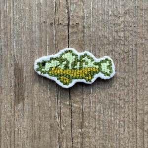 May include: A green and yellow embroidered fish patch. The fish is outlined in white and has a yellow belly.