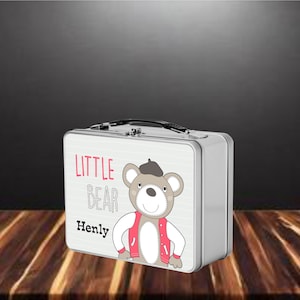 May include: A silver metal lunchbox with a white background and a cartoon bear wearing a red jacket and a beret. The text "LITTLE BEAR" and "Henly" are printed on the lunchbox.