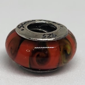 May include: A round bead with a silver-colored metal ring. The bead is primarily orange with swirling patterns of brown and yellow. The metal ring has the text "925" and other markings.