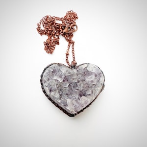 May include: A copper wire heart-shaped pendant with a clear amethyst crystal inside. The pendant is attached to a copper chain.