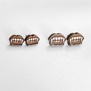 May include: A pair of wooden earrings shaped like fangs. The earrings are brown with white accents.