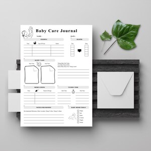 Puede incluir: Un Diario de Cuidado del Bebé blanco con secciones para la alimentación, el sueño, los medicamentos y el tiempo de barriga. El diario incluye espacio para registrar el estado de ánimo del bebé y notas para la madre. Un sobre blanco y hojas verdes están junto al diario.