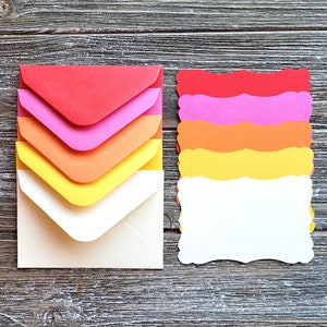 May include: A set of five colorful envelopes with scalloped edges and a white envelope with a pointed flap. The envelopes are stacked in a graduated color scheme from red to yellow.