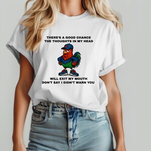 May include: White t-shirt featuring a cartoon rooster wearing a blue cap and sneakers. The rooster has red, blue, and green accents. Text on the shirt reads: "THERE'S A GOOD CHANCE THE THOUGHTS IN MY HEAD WILL EXIT MY MOUTH DON'T SAY I DIDN'T WARN YOU."