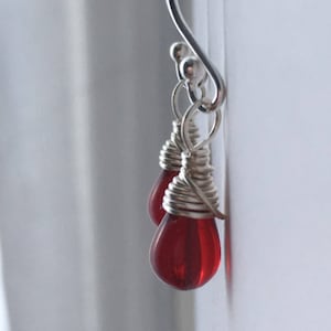 May include: Silver dangle earrings with a red glass teardrop pendant wrapped in silver wire.