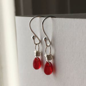 May include: A pair of silver dangle earrings with red glass teardrop beads.