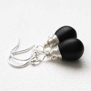 May include: A pair of black teardrop-shaped earrings with silver wire wrapped around the top of each teardrop. The earrings are attached to silver hooks.