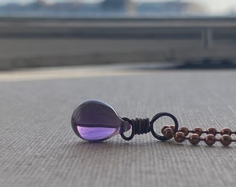 May include: A purple glass teardrop pendant on a copper chain necklace.