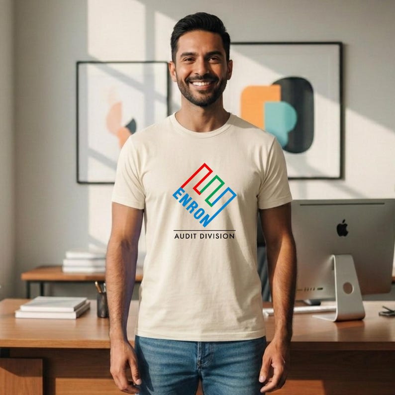 May include: A cream-colored t-shirt with the word "ENRON" in a colorful logo, with the words "AUDIT DIVISION" below. The shirt is worn by a person in blue jeans.