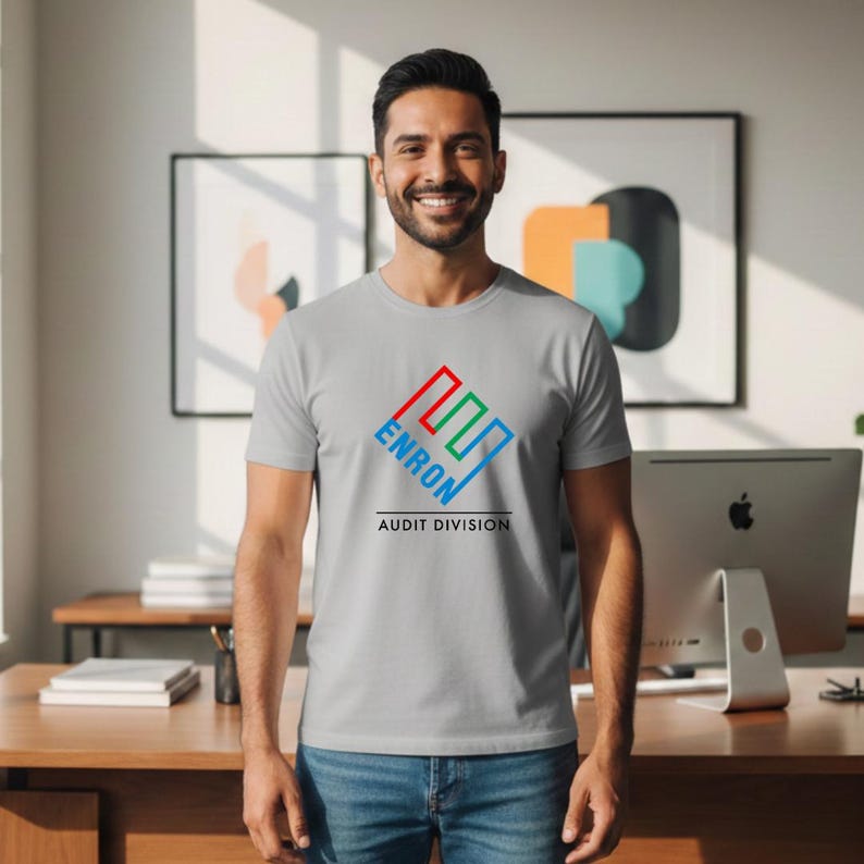 May include: A light gray t-shirt with the word "ENRON" in a colorful logo, with "AUDIT DIVISION" below. The shirt is worn by a person in blue jeans.