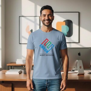 May include: A light blue t-shirt with the word "ENRON" in a red, green, and blue geometric design. Below the design, the text reads "AUDIT DIVISION". The shirt is worn by a person.