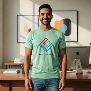 May include: A light green t-shirt with the text "ENRON AUDIT DIVISION" in red, green, and blue. The shirt is short-sleeved and made of a soft material. The person is wearing blue jeans.