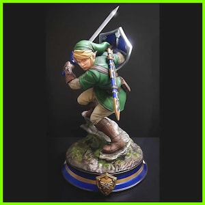Op de afbeelding: Een groen en bruin beeldje van Link uit de Legend of Zelda-videogameserie. Hij houdt een zwaard en schild vast en staat op een rotsvoet. De voet is versierd met een gouden en blauw ontwerp.