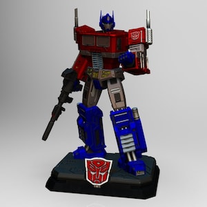 Op de afbeelding: Een rood en blauw robot-actiefiguur dat op een zwarte basis staat met een rood Autobot-symbool. De robot houdt een zwart pistool in zijn rechterhand.