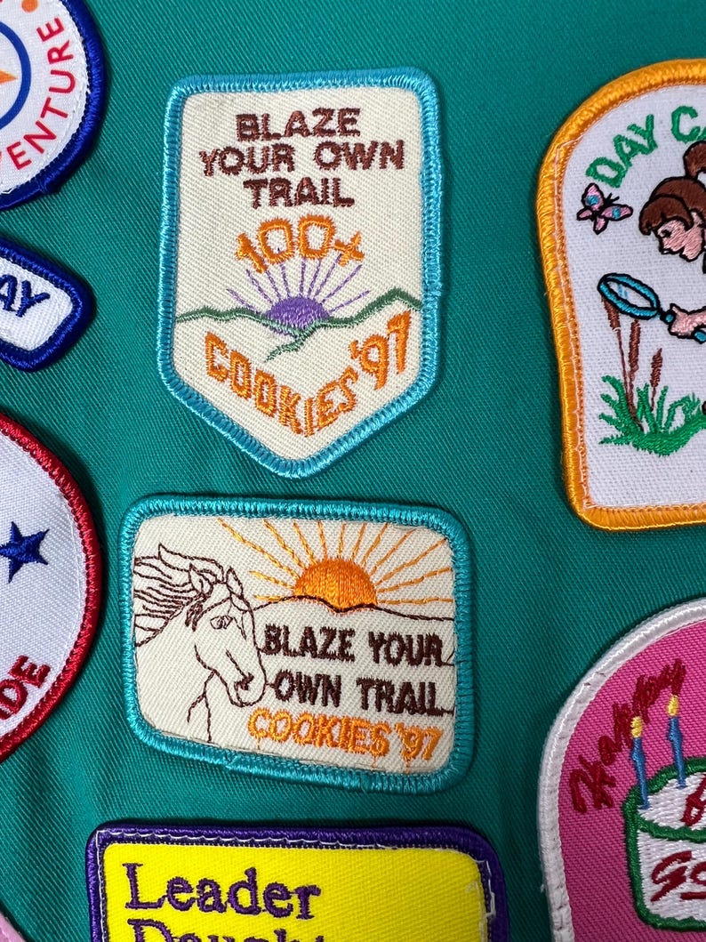 May include: Assortment of embroidered patches with various designs and text. One patch reads "BLAZE YOUR OWN TRAIL COOKIES '97" with a horse and sun graphic. Other patches include text like "ADVENTURE" and "DAY CAMP".
