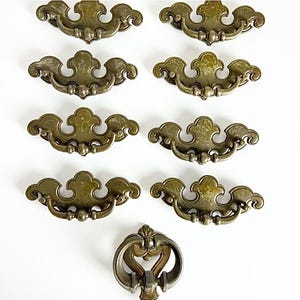 May include: Set of ten antique brass cabinet knobs with a decorative, ornate design. The knobs have a slightly tarnished finish and are in good condition.
