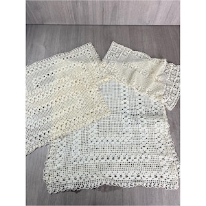 May include: A set of three off-white rectangular crochet doilies featuring intricate openwork patterns with geometric and floral motifs. Each piece displays a delicate, hand-crafted lace design with scalloped edges and a fine, airy texture.
