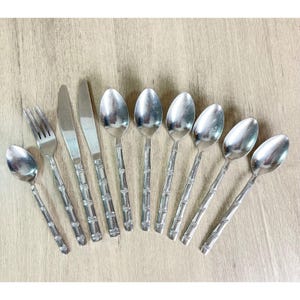 May include: A set of nine stainless steel flatware pieces including one fork, two knives, and six spoons. Each utensil features a decorative handle designed to resemble segmented bamboo stalks with a polished, reflective metallic finish.