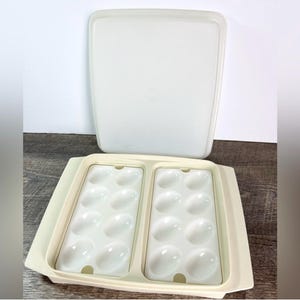 May include: A vintage, off-white deviled egg serving dish with a matching lid. The dish has two sections, each with oval indentations to hold eggs. The lid is rectangular and slightly translucent.