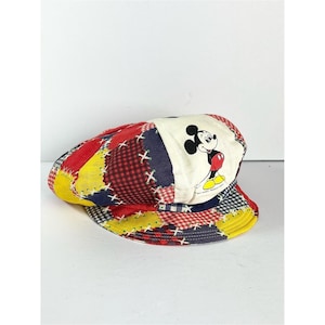 May include: A patchwork newsboy cap featuring a Mickey Mouse graphic. The cap has a multi-colored design with red, yellow, blue, and white patches. The Mickey Mouse graphic is on a white patch.