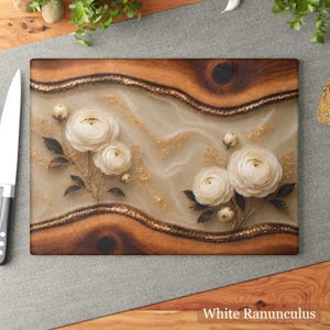 K&ouml;nnte beinhalten: Rechteckiges Holzschneidebrett mit wei&szlig;em und goldenem Blumendesign. Das Brett hat eine hellfarbene Mitte mit wei&szlig;en Ranunkelbl&uuml;ten und goldenen Akzenten, umrahmt von dunklem Holz und einem goldenen Rand. Der Text "White Ranunculus" befindet sich unten.