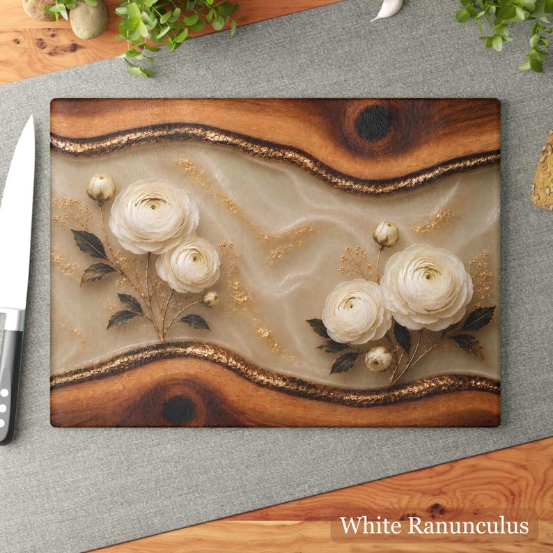 K&ouml;nnte beinhalten: Rechteckiges Holzschneidebrett mit wei&szlig;em und goldenem Blumendesign. Das Brett hat eine hellfarbene Mitte mit wei&szlig;en Ranunkelbl&uuml;ten und goldenen Akzenten, umrahmt von dunklem Holz und einem goldenen Rand. Der Text "White Ranunculus" befindet sich unten.