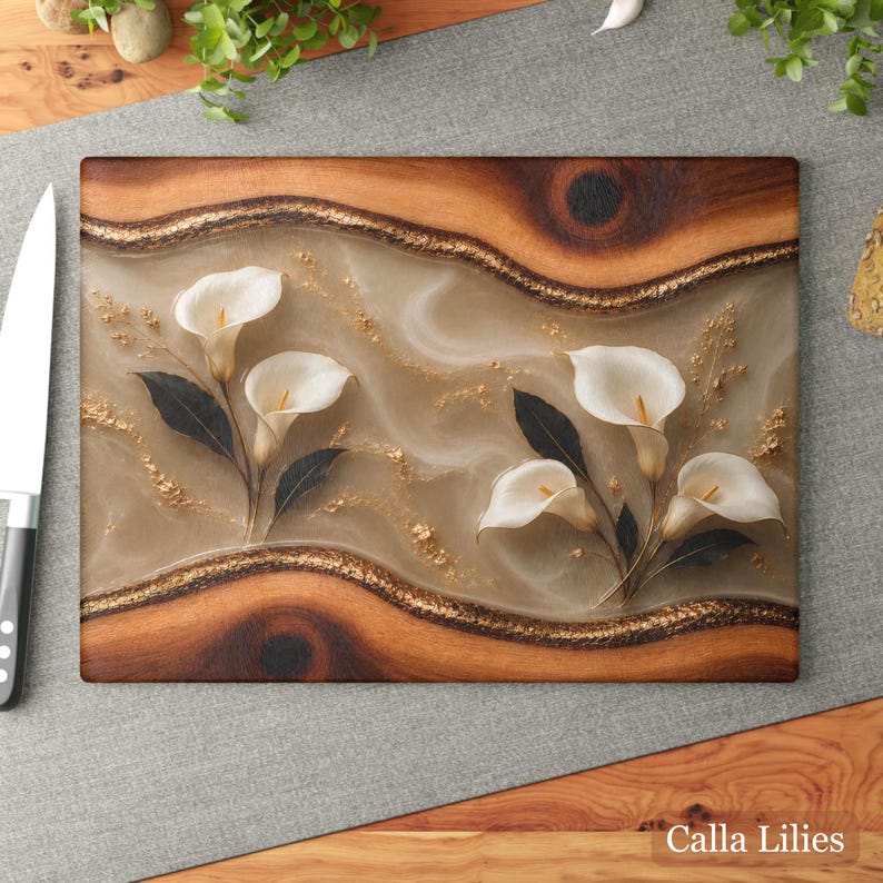 K&ouml;nnte beinhalten: Rechteckiges Holzschneidebrett mit einem dekorativen Design mit wei&szlig;en Calla-Lilien und dunkelgr&uuml;nen Bl&auml;ttern. Das Brett hat einen hellbraunen Hintergrund mit goldenen Akzenten und dem Text "Calla Lilies".