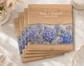 Peut inclure: Un ensemble de quatre sous-verres carrés en bois avec une finition grain de bois brun clair. Chaque sous-verre présente une bande horizontale centrale avec un motif floral d'hortensias bleus et le texte Noah & Hannah 04.14.2026 imprimé en haut.