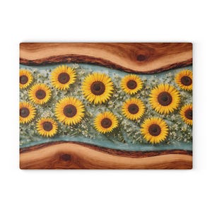 Peut inclure: Une planche &agrave; d&eacute;couper rectangulaire compos&eacute;e de deux tranches de bois naturel &agrave; bord brut en haut et en bas, s&eacute;par&eacute;es par une incrustation centrale en r&eacute;sine bleu clair translucide remplie de tournesols jaunes et de petites fleurs blanches.