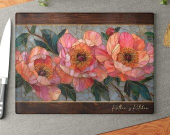 Peut inclure: Une planche à découper rectangulaire en bois avec un panneau central orné d'un motif floral de pivoines roses et orange façon vitrail. La planche présente des bordures en bois foncé en haut et en bas, avec le texte Kathie's Kitchen en doré.