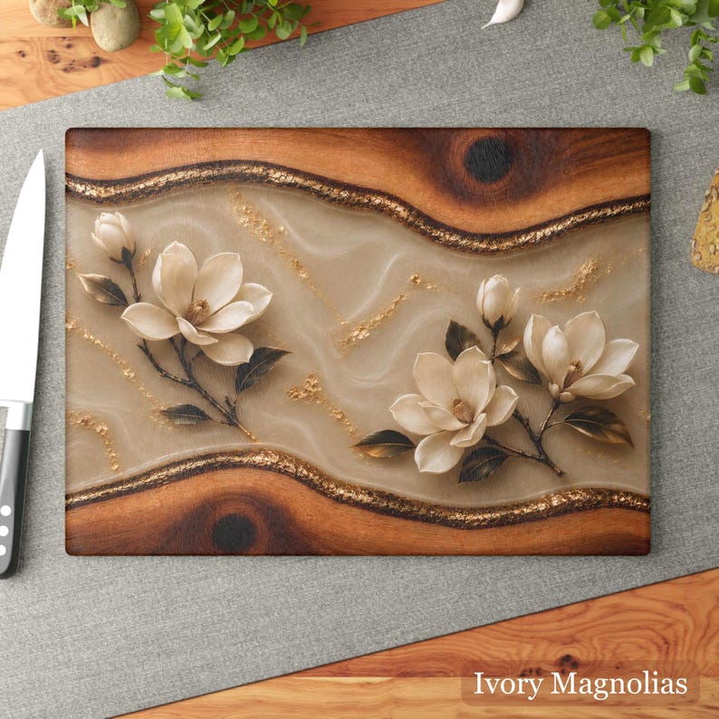 K&ouml;nnte beinhalten: Rechteckiges Holzschneidebrett mit hellbeiger Mitte und dekorativem Rand. Die Mitte zeigt elfenbeinfarbene Magnolienbl&uuml;ten und goldene Akzente. Der Text "Ivory Magnolias" befindet sich unten.