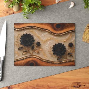 K&ouml;nnte beinhalten: Rechteckiges Holzschneidebrett mit dekorativem Blumendesign. Das Brett hat einen cremefarbenen Mittelteil mit goldenen Akzenten und zwei schwarzen Blumendesigns mit goldenen Bl&auml;ttern. Die R&auml;nder sind aus dunkelbraunem Holz.