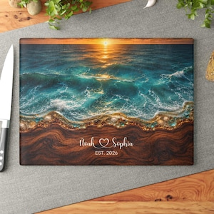 Könnte beinhalten: Ein rechteckiges Glasschneidebrett mit einer Ozean-Sonnenuntergangsszene, bei der türkisfarbene Wellen auf ein dunkles Holzmaserung-Ufer treffen. Das Design enthält Muscheln und den weißen Text Noah & Sophia mit dem Datum EST. 2026.