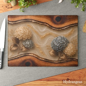 K&ouml;nnte beinhalten: Rechteckiges Holzschneidebrett mit floralem Design. Das Brett hat einen braunen Holzrahmen mit einem zentralen Design aus Beige- und Goldakzenten sowie drei Hortensienbl&uuml;tenclustern in Beige und Blau. Das Wort "Hydrangeas" steht unten.