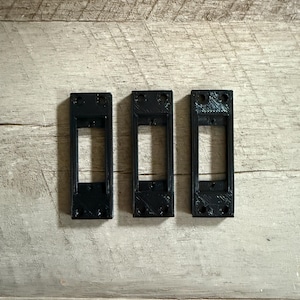 May include: Three black plastic wall plate covers with rectangular openings. The plates are arranged horizontally in a row.
