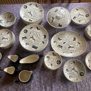 Può includere: Un servizio di piatti vintage moderno della metà del secolo. Il set comprende piatti, ciotole, piatti da portata e tazze. Le stoviglie bianche e grigie presentano un design astratto nero di mobili e utensili. Il set è disposto su una tovaglia viola.