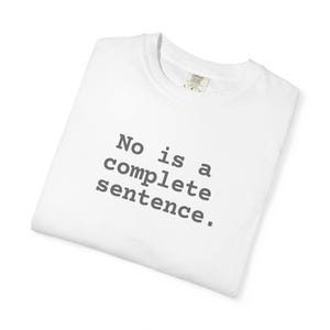 Puede incluir: Una camiseta blanca con la frase "No is a complete sentence" impresa en gris. La camiseta está doblada cuidadosamente, con el cuello y la etiqueta visibles. El texto está centrado en la parte delantera de la camiseta.
