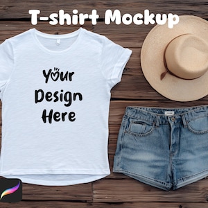 May include: A white t-shirt mockup with the text "Your Design Here" in black, a straw hat, and denim shorts on a wooden surface. The t-shirt is the focal point, with the hat and shorts arranged nearby. The image also includes the Photoshop and Procreate icons.