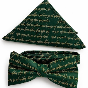 May include: A dark green bow tie and a matching folded pocket square. Both items feature a repeating pattern of gold-colored script text printed across the fabric surface. The bow tie is pre-tied with a central knot and adjustable strap.
