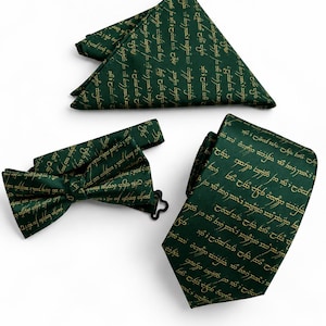 May include: A dark green necktie, a bow tie with a black adjustable hook, and a folded pocket square. Each item features a repeating pattern of gold-colored script text printed across the fabric surface, creating a cohesive set of formal accessories.