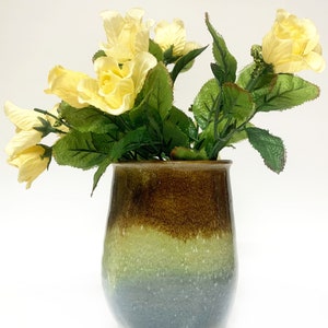 May include: A ceramic vase with a brown, green, and blue glaze. The vase is filled with a bouquet of yellow roses.