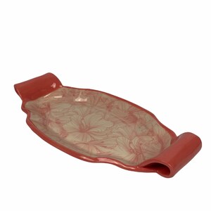 Può includere: Un vassoio da portata in ceramica rossa con un motivo floreale. Il vassoio ha due manici sui lati.