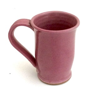 May include: A pink ceramic mug with a rounded handle. The mug has a smooth, slightly textured surface.