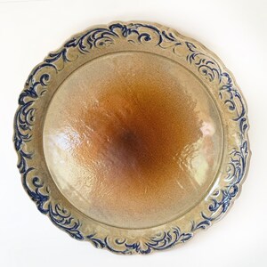 Può includere: Un grande piatto rotondo in ceramica con una glassa marrone e un motivo floreale blu intorno al bordo.