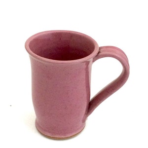 May include: A pink ceramic mug with a rounded body and a handle. The mug has a speckled glaze.
