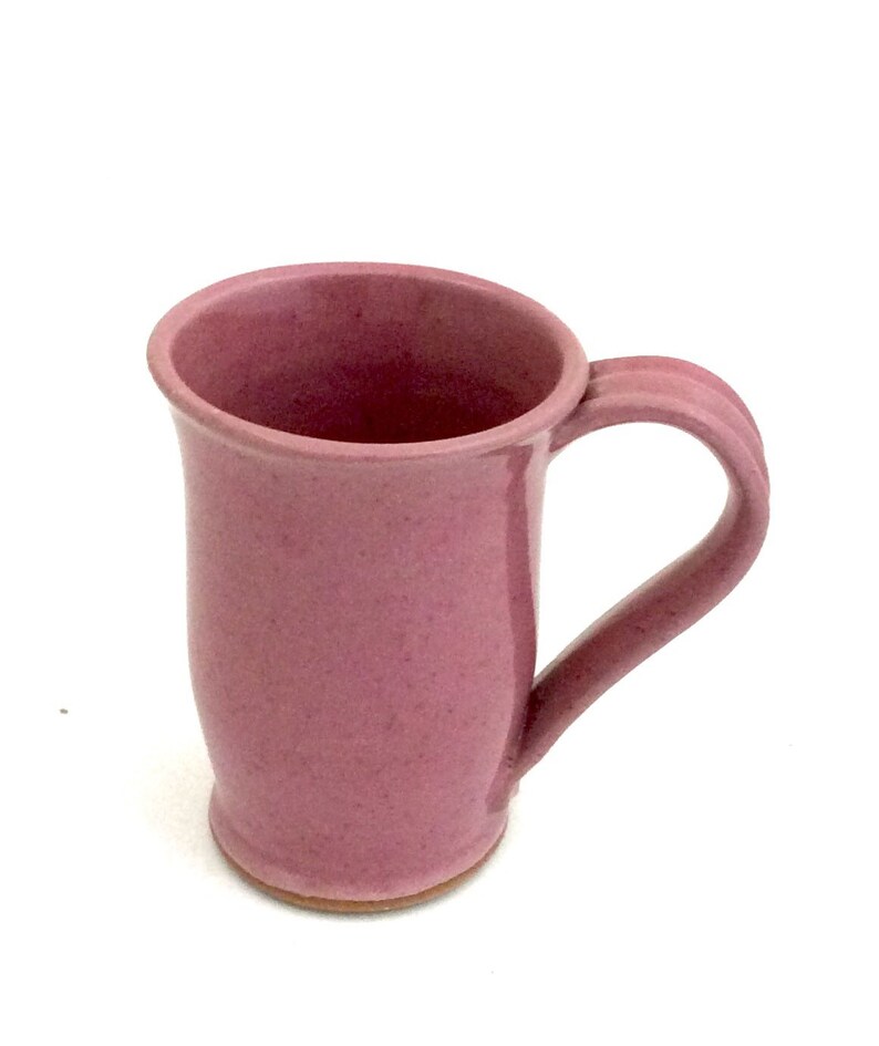 May include: A pink ceramic mug with a rounded body and a handle. The mug has a speckled glaze.