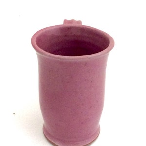 May include: A pink ceramic mug with a rounded shape and a small handle. The mug has a smooth, slightly textured surface.