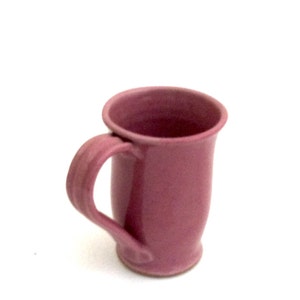 May include: A pink ceramic mug with a rounded handle. The mug has a smooth, glossy finish.