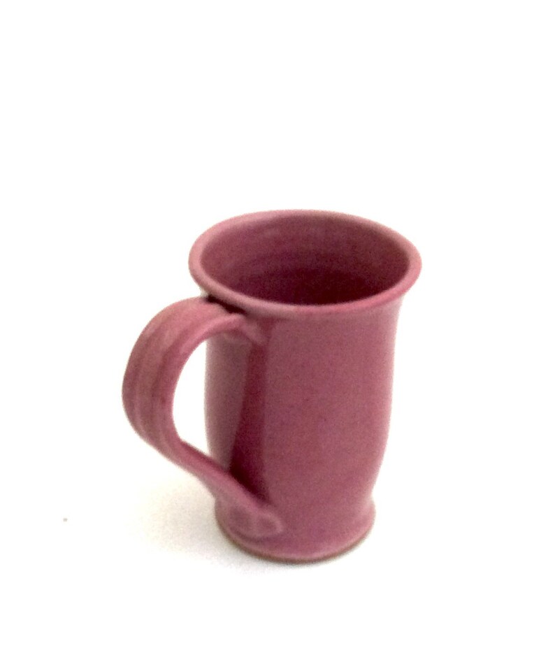 May include: A pink ceramic mug with a rounded handle. The mug has a smooth, glossy finish.